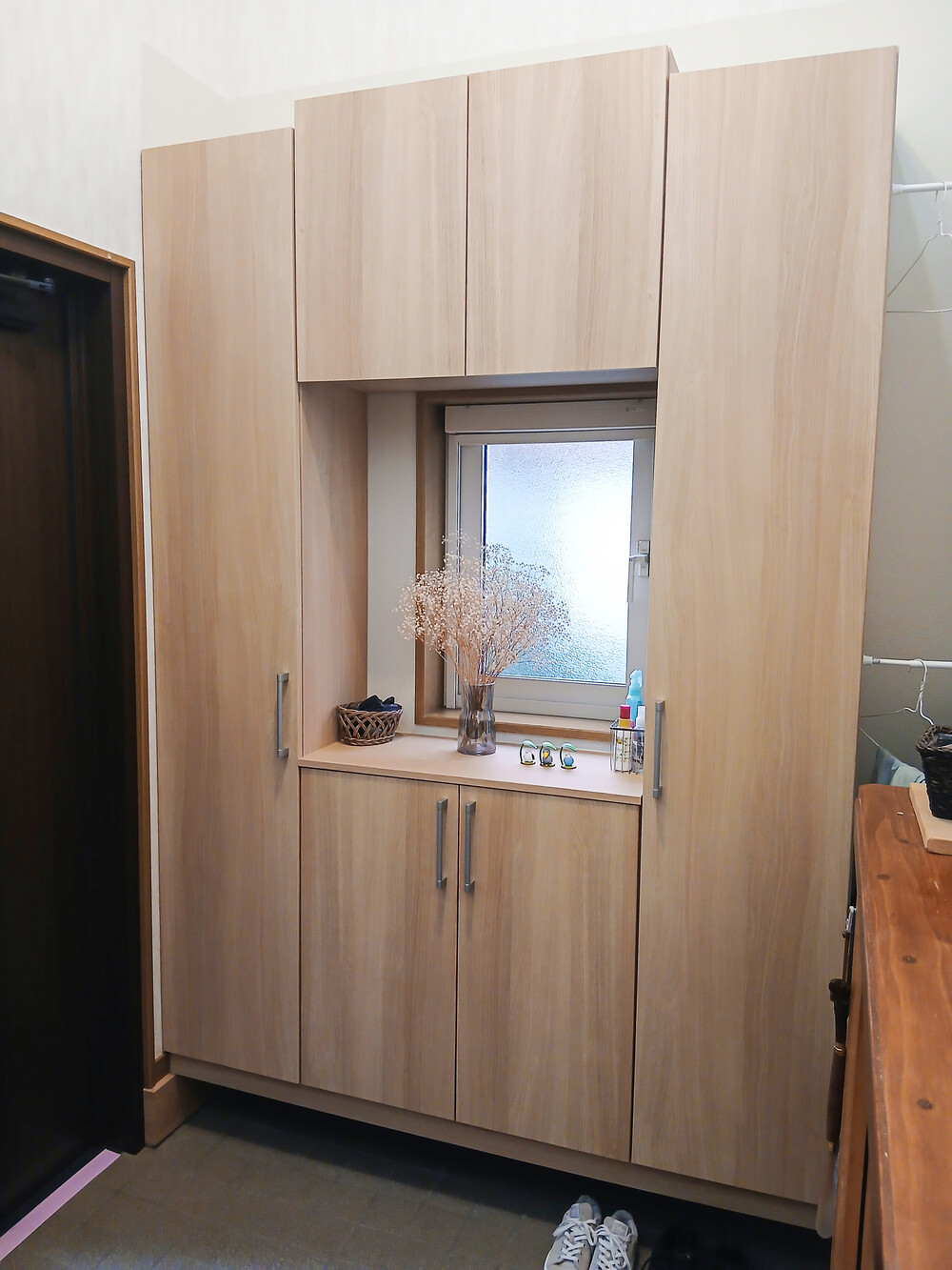 窓の明かりを活かしたまま、収納量を最大化。明るいカラーで空間が広く感じられ、散らかりがちな玄関がスッキリ整いました。