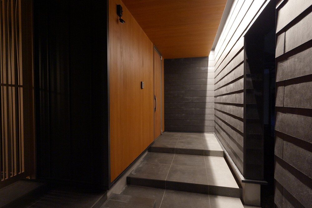 屋根を付け、樹木を撤去し、坪庭だった場所へコンクリートを打設し玄関アプローチへ。人感センサー付き間接照明でアプローチを演出する事で奥行き有る空間へ。