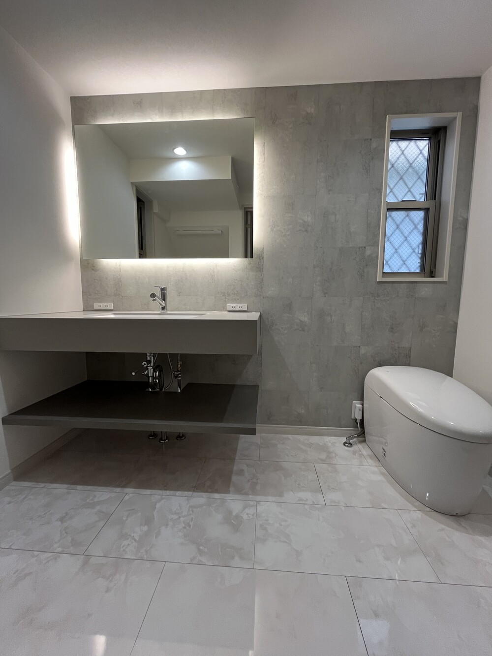 コンクリート調のクロスに鏡面仕上げのフロアを合わせた、高級感のある洗面空間。大きな鏡が印象的です。