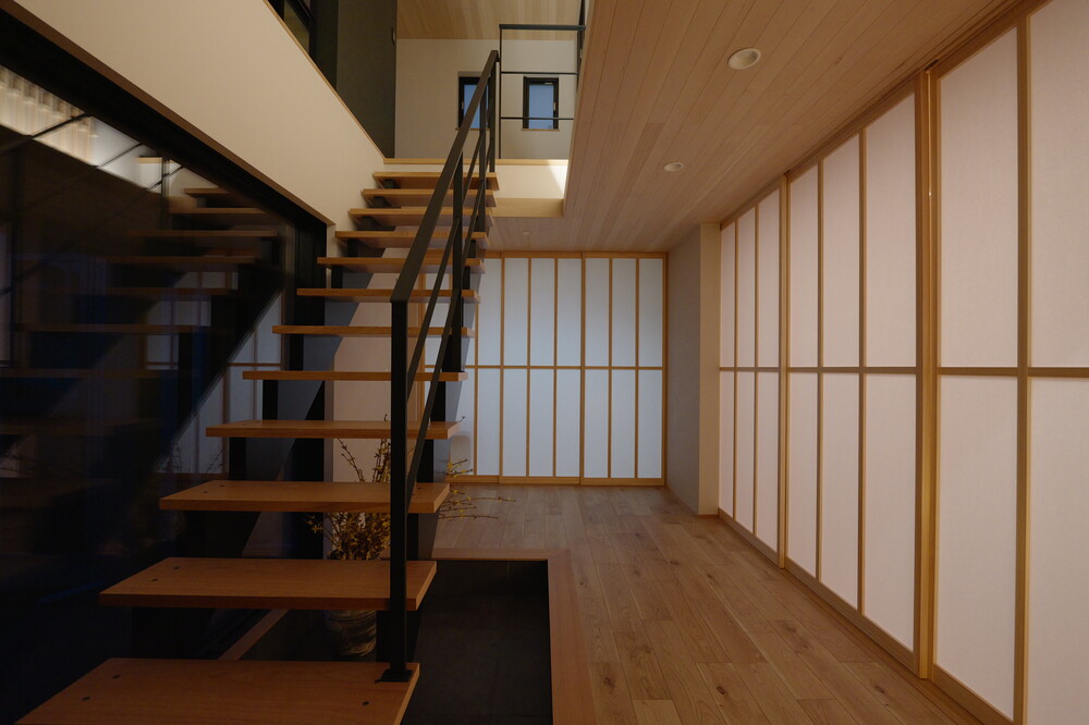 南側（既存リビング）を玄関ホールの一部として階段を移設。蓄熱土間タイル仕様として日射熱を吹き抜けを使いコントロールできる空間へ。また来客者から見た開放感も演出できます。障子を開ければ土間テラスとしてLDKと一体で利用、障子を閉めれば和室へ来客を直接案内できるホールとしても利用可能な可変性のある空間へ改修。