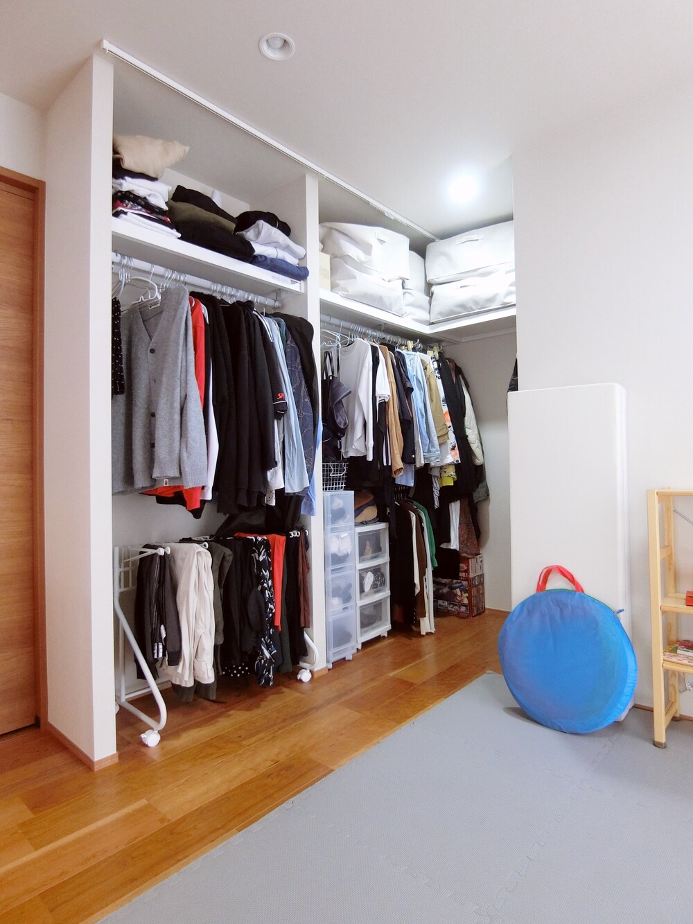 リビングや洋室側からはL字型に見える収納スペース。奥をのぞくとコの字型に広がり、一角に設けた可動棚で小物類もすっきりと整理できます。天井にはカーテンレールを設置し、必要に応じて目隠しができるよう配慮しました。